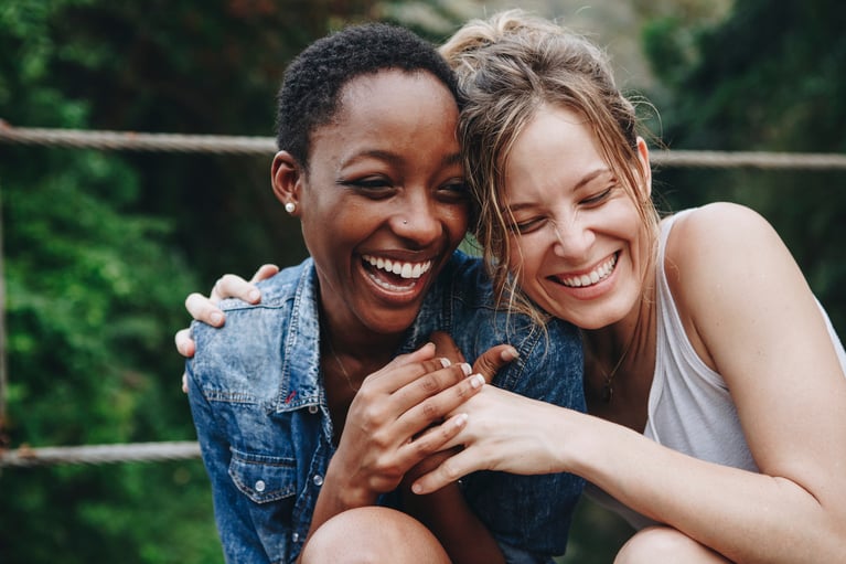 Primer plano de dos mujeres jovenes abrazándose y sonriendo al aire libre, en el contexto del uso de anticonceptivos.jpg