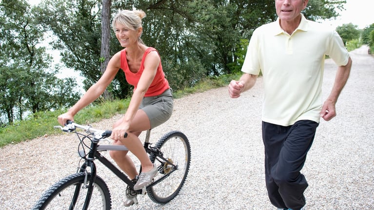 Dos personas haciendo ejercicio al aire libre — una en bicicleta y otra corriendo — actividad física para la prevención cardiovascular