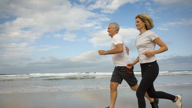 Dos personas corriendo juntas en la playa, actividad física al aire libre y estilo de vida saludable relacionado con la salud cardiovascular
