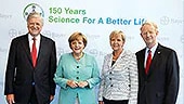 Imagem mostrando quatro pessoas em trajes formais posicionadas diante de um fundo com a inscrição “150 Years – Science For A Better Life”, representando a comemoração do 150º aniversário da Bayer e a fase de investimento no futuro entre 2010 e 2015.