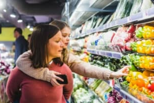 Woman with girl in front of vegetable shelf in supermarket
