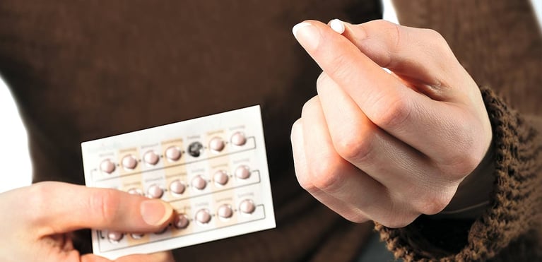 Manos sosteniendo un blíster de píldoras anticonceptivas y una pastilla entre los dedos.