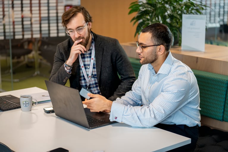 Two professionally dressed colleagues wearing glasses collaborating on a laptop in a modern, bright office space focused on efficient teamwork.