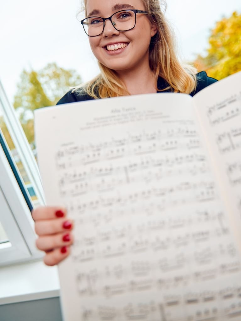 Person holding a sheet of music outdoors, representing Bayer’s cultural programs and support for arts and music.