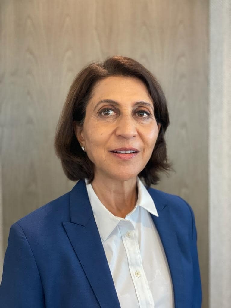 Profile photo of Radhika Rajan in a professional blue blazer and white shirt, posing against a wooden background.
