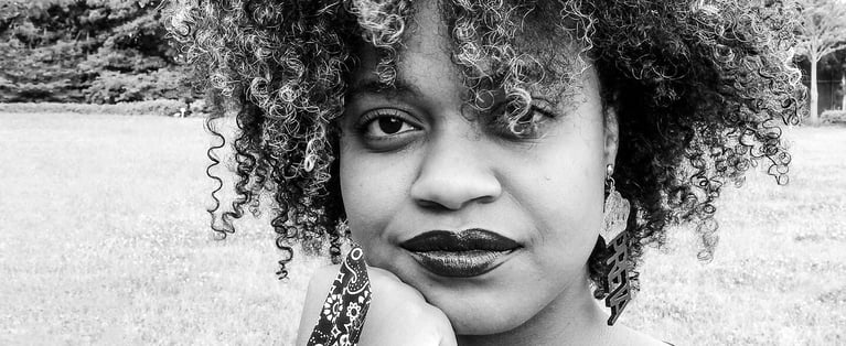  Black-and-white portrait of a woman with curly hair outdoors, looking at the camera.