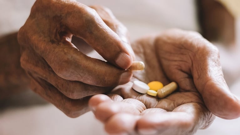 Pills in a seniors hand 1440x590