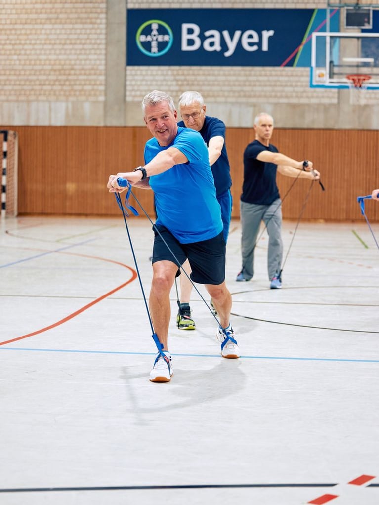 People exercising with resistance bands in an indoor sports hall, representing Bayer’s sports and cultural clubs.