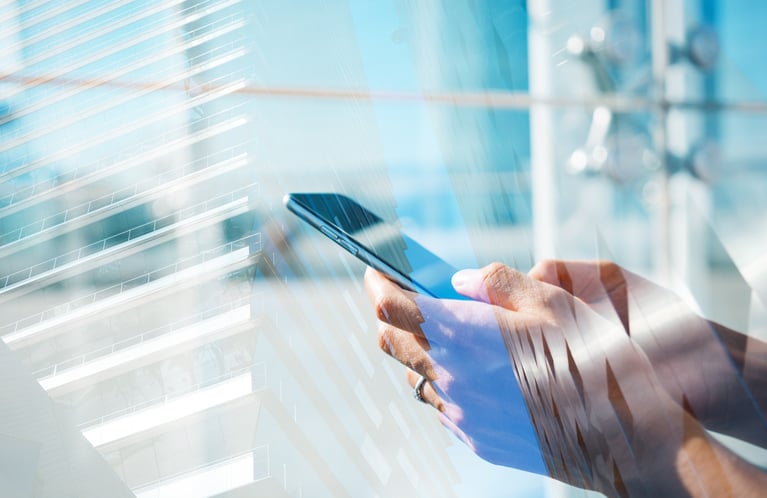 A double exposure image overlaying a close-up of hands holding a smartphone with a bright, glass-facade modern office building.