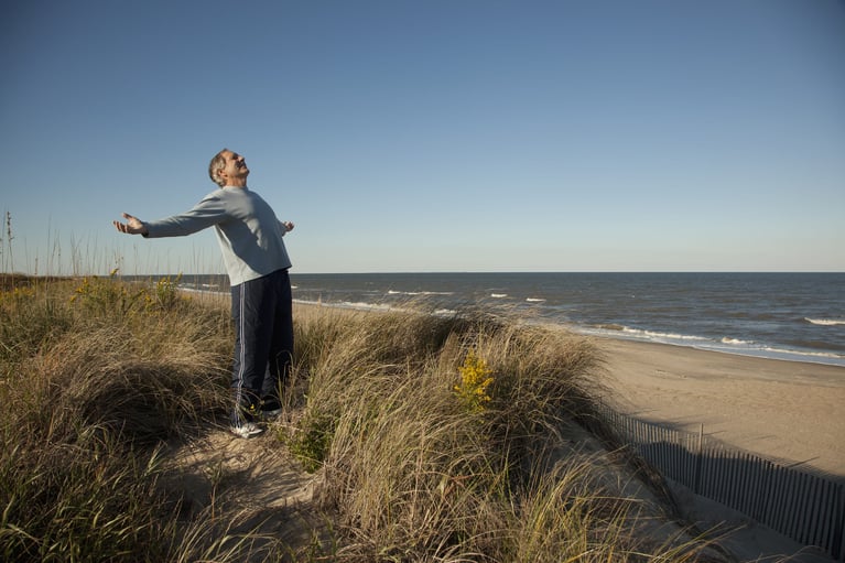 Persona de pie junto al mar con los brazos abiertos, estilo de vida saludable y bienestar como parte de la prevención y el cuidado de la salud masculina