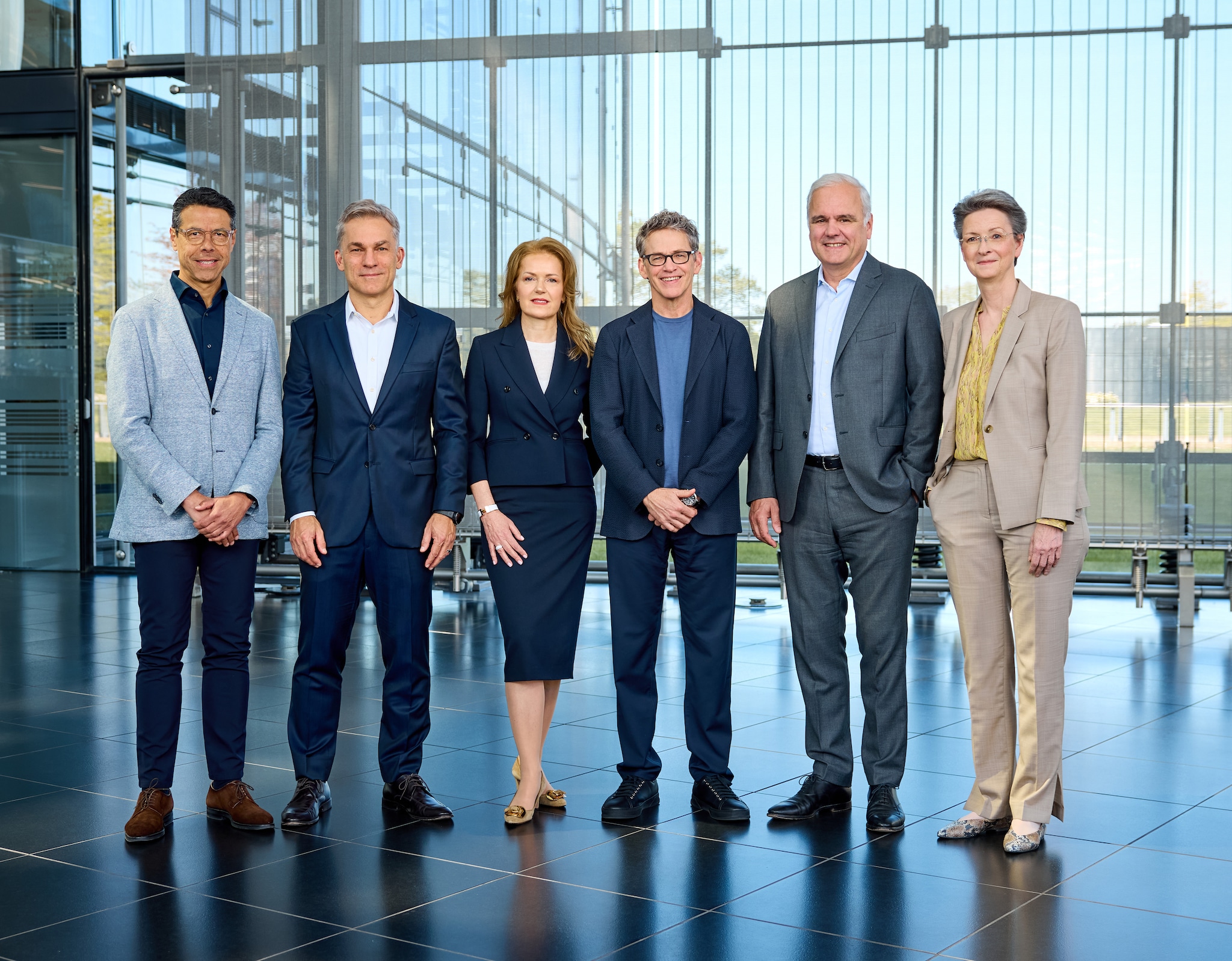 Group photo of the members of the Bayer Board of Management in a bright, glass-walled building. From left to right: Julio Triana, Rodrigo Santos, Judith Hartmann, Bill Anderson, Stefan Oelrich, and Heike Prinz.